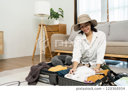 Woman Packing Suitcase for Travel in Cozy Living Room with Modern Furniture and Natural Light Woman Packing Suitcase for Travel in Cozy Living Room with Modern Furniture and Natural Light 128368934