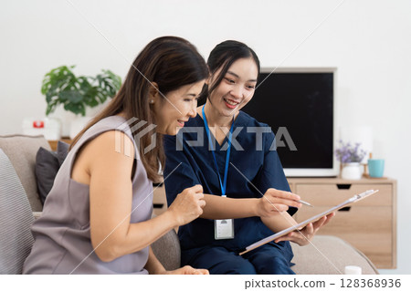 Healthcare Professional Providing In-Home Care and Consultation to a Smiling Patient in a Modern Living Room Setting Healthcare Professional Providing In-Home Care and Consultation to a Smiling Patient in a Modern Living Room Setting 128368936