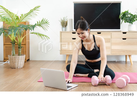 Young Woman Practicing Yoga at Home with Laptop and Dumbbells for a Healthy Lifestyle and Wellness Routine 128368949