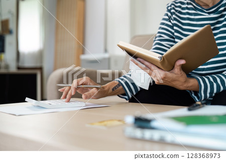 Senior Adult Managing financial at Home with Notebook and Calculator, Planning Budget and Paying Bills Senior Adult Managing financial at Home with Notebook and Calculator, Planning Budget and Paying Bills 128368973
