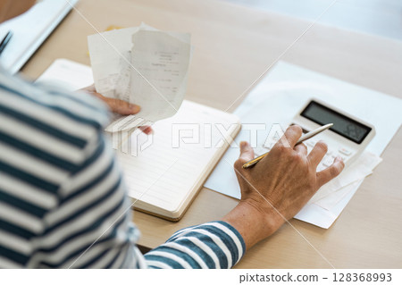 Senior Retirement Planning - Elderly Person Calculating Finances with Calculator and Receipts at Home Senior Retirement Planning - Elderly Person Calculating Finances with Calculator and Receipts at Home 128368993