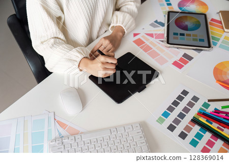 Creative Designer Working on Digital Tablet Surrounded by Color Swatch and Design Tools in Modern Workspace Creative Designer Working on Digital Tablet Surrounded by Color Swatch and Design Tools in Modern Workspace 128369014