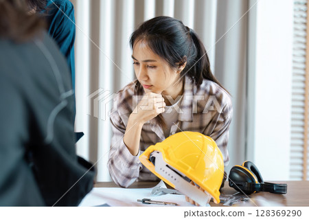 Female Engineer in Plaid Shirt Working on Construction Project with Safety Gear on Desk 128369290