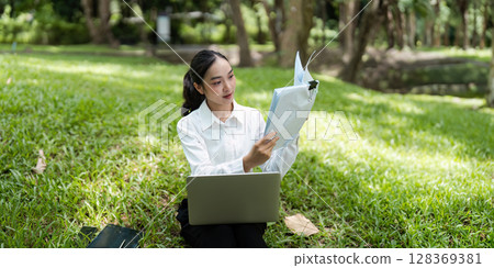 Young Business Woman Digital Nomad Working Outdoors with Laptop and Documents in a Park Setting 128369381
