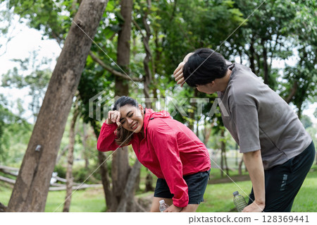 Two Friends Taking a Break from Jogging in a Lush Green Park, Smiling and Enjoying the Outdoors on a Sunny Day Two Friends Taking a Break from Jogging in a Lush Green Park, Smiling and Enjoying the Outdoors on a Sunny Day 128369441