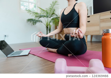 Woman Practicing Yoga at Home for Wellness with Laptop and Exercise Equipment in Modern Living Room Woman Practicing Yoga at Home for Wellness with Laptop and Exercise Equipment in Modern Living Room 128369466