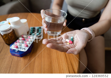 Close-Up of Person Holding Various Pills and a Glass of Water, Healthcare and Medication Concept Close-Up of Person Holding Various Pills and a Glass of Water, Healthcare and Medication Concept 128369552