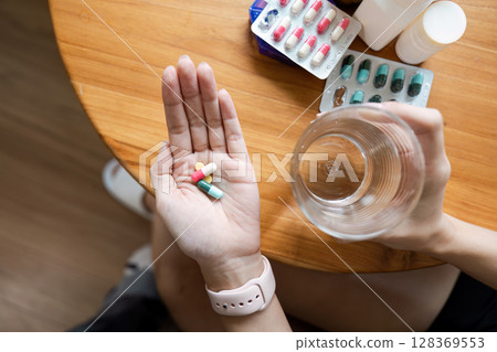 Close-Up of Hand Holding Pills with Glass of Water on Wooden Table - Healthcare and Medication Concept Close-Up of Hand Holding Pills with Glass of Water on Wooden Table - Healthcare and Medication Concept 128369553