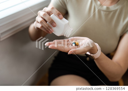 Woman Pouring Pills from a Bottle into Her Hand - Concept of Healthcare, Medication, and Wellness 128369554