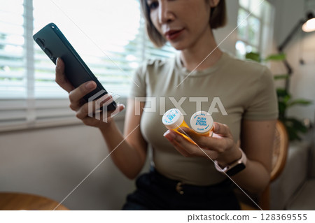 Woman Checking Prescription Pills on Smartphone for Healthcare Information in Modern Home Setting Woman Checking Prescription Pills on Smartphone for Healthcare Information in Modern Home Setting 128369555