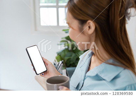 Young Professional Woman Working from Home, Holding Smartphone and Coffee Mug, Remote Work Concept 128369580