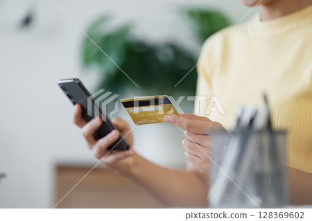 Woman Using Credit Card for Online Shopping on Smartphone in Modern Home Setting 128369602