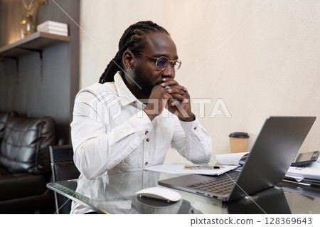 Focused Professional Working from Home on Laptop with Documents and Coffee in Modern Home Office Setting 128369643