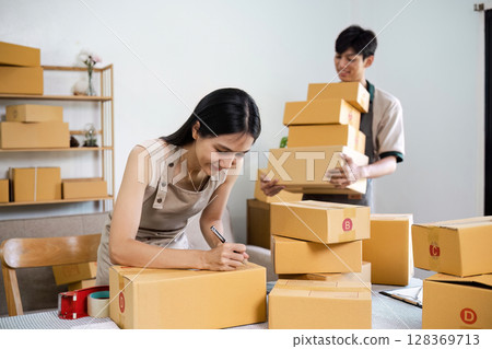 Small Business Owners Preparing Online Order for Shipment in Home Office with Cardboard Boxes and Smiling Faces 128369713