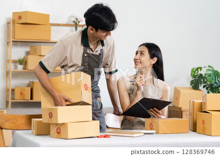 Young Entrepreneur management Online Orders in a Small Business Office with Cardboard Boxes and Clipboard 128369746