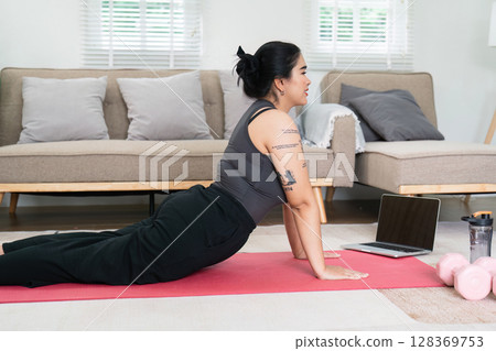 Overweight Woman Practicing Yoga at Home for Wellness and Fitness with Laptop and Dumbbells Overweight Woman Practicing Yoga at Home for Wellness and Fitness with Laptop and Dumbbells 128369753