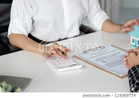 Real Estate Agent Calculating Mortgage Costs with Client, Loan Agreement on Desk Real Estate Agent Calculating Mortgage Costs with Client, Loan Agreement on Desk 128369754