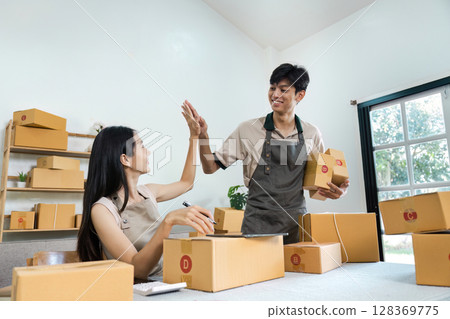 Young Entrepreneur Celebrating Success in Small Business with Shipping Boxes in Modern Home Office 128369775