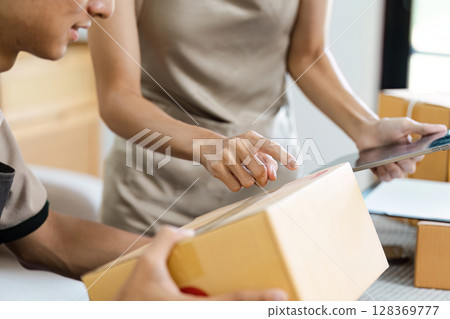 Small Business owner Managing order and Inventory Using Digital Tablet and Cardboard Boxes in Modern Workspace 128369777