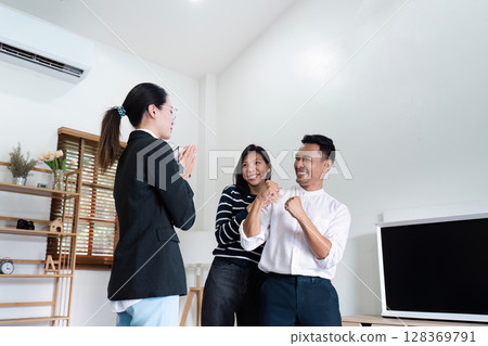 Real Estate Agent Celebrating with Happy Couple Clients in Modern Living Room After Successful Home Purchase Real Estate Agent Celebrating with Happy Couple Clients in Modern Living Room After Successful Home Purchase 128369791