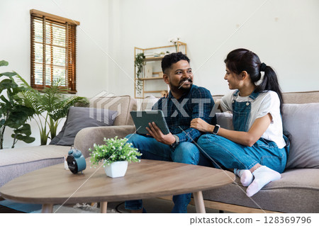 Happy Indian Couple Relaxing at Home with Tablet, Smiling and Enjoying Quality Time Together on the Couch 128369796