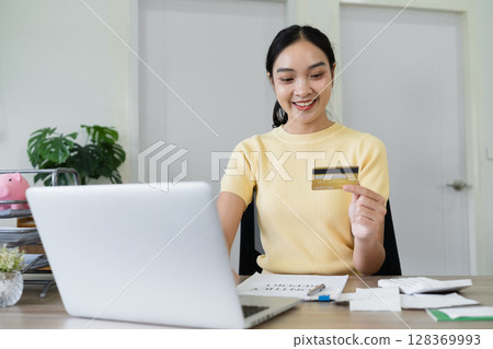 Young Woman Holding Credit Card While Using Laptop for Online Banking and Shopping at Home Office Young Woman Holding Credit Card While Using Laptop for Online Banking and Shopping at Home Office 128369993