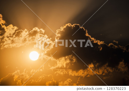 Bright sun shining through dramatic golden clouds with sun rays piercing the sky during a moody sunset or sunrise 128370223