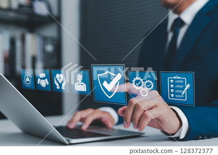 Work Safety and Compliance Concept. Businessman using laptop with icons safety, compliance, quality control, and risk management, representing workplace safety, regulations, and operational standards. 128372377