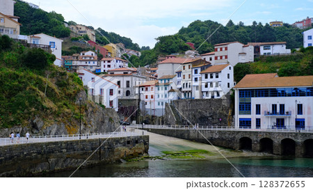 A picturesque view of a charming coastal village nestled into a hillside, with colorful traditional houses cascading down towards a tranquil harbor. Cudillero, Spain 128372655