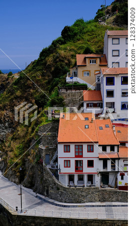 A captivating vertical shot of the charming village of Cudillero, Asturias, Spain, showcasing its traditional houses built into a steep hillside. 128374009