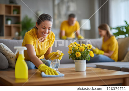 Woman with mysophobia happily cleaning wooden table using disinfect spray while others clean living room to prevent virus spread 128374731