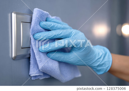 Cleaning light switch with cloth and glove shows mysophobia care to disinfect surfaces and prevent virus spread in clean environment 128375006