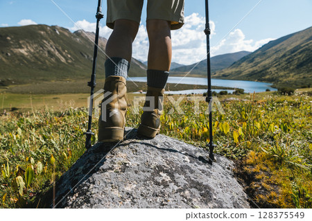 Hiker legs wearing leather boots hiking on high altitude mountain top,with a lake in the distance Hiker legs wearing leather boots hiking on high altitude mountain top,with a lake in the distance 128375549