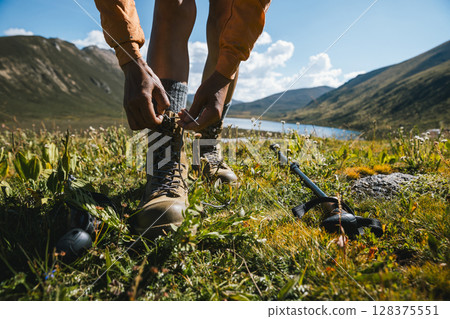 Hiker tying shoelace of leather hiking boots on high altitude mountain top,with a lake in the distance 128375551