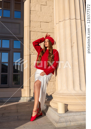 Fashion Model Column: Woman in red sweater posing by pillar, daytime, for artistic portrait outdoors. 128377572