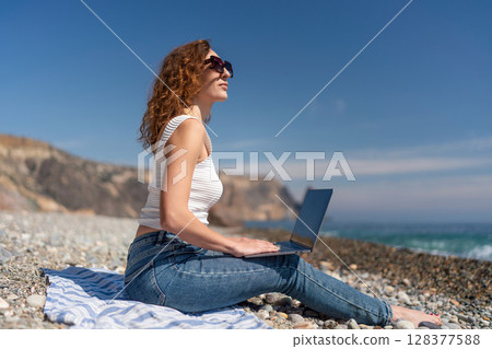 Beach Laptop Woman working remotely by ocean on sunny day for flexibility. Beach Laptop Woman working remotely by ocean on sunny day for flexibility. 128377588