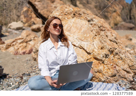 Beach Laptop Woman: Works outside on sunny day sitting near rocks in spring. Beach Laptop Woman: Works outside on sunny day sitting near rocks in spring. 128377589
