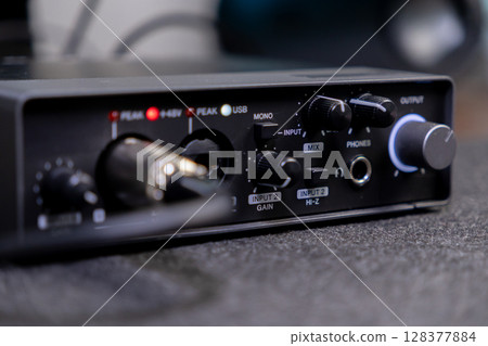 Compact black audio interface with various control knobs, input ports, and text labels like PHONES and OUTPUT, essential for home studio music production setups 128377884