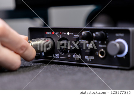 A hand expertly connects an XLR audio cable into the D-PRE MICLINE input of a compact black sound interface, demonstrating professional setup for high-fidelity recording or live streaming 128377885