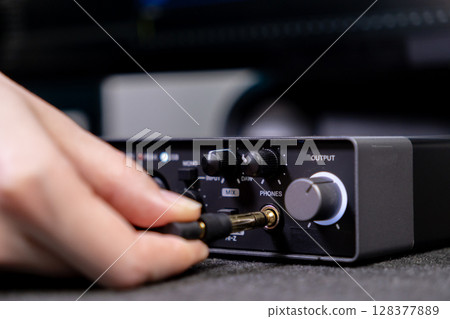 Hand plugging an audio jack into a digital audio interface, illustrating music production and sound engineering setup for a modern home studio 128377889
