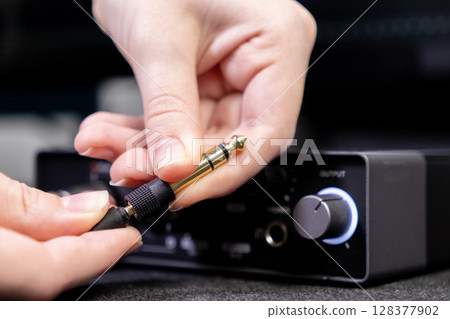 Close-up of human hands precisely plugging a shiny gold-tipped audio jack into a black output port on a professional sound interface for quality music production Close-up of human hands precisely plugging a shiny gold-tipped audio jack into a black output port on a professional sound interface for quality music production 128377902