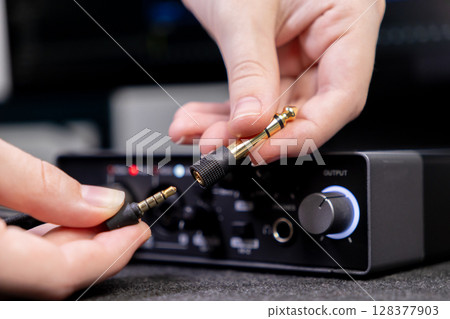 Hand holds a gold-plated audio jack adapter, connecting a cable to an audio interface for professional sound recording and music production Hand holds a gold-plated audio jack adapter, connecting a cable to an audio interface for professional sound recording and music production 128377903
