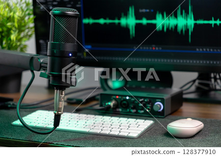 Black studio microphone on a desk with a computer monitor showing a green audio waveform, perfect for podcasting, music production, and content creation 128377910