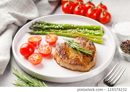 Grilled beef steak closeup with asparagus and cherry tomatoes on white plate, gourmet healthy dinner 128378232