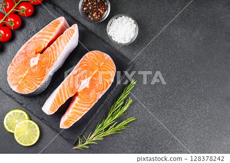 Two fresh raw salmon steaks with tomatoes, spices, rosemary and lime on black stone background 128378242