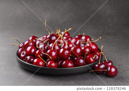 Black plate full of fresh ripe red sweet cherry on dark gray texured bakground 128378246
