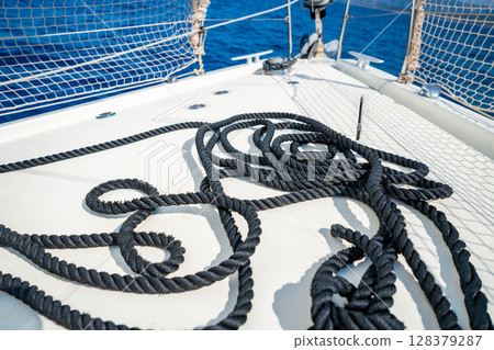 Black rope lying on the bow of a sailing yacht moving under full sails near Croatia. Marine detail, navigation, strength and motion at sea. Black rope lying on the bow of a sailing yacht moving under full sails near Croatia. Marine detail, navigation, strength and motion at sea. 128379287