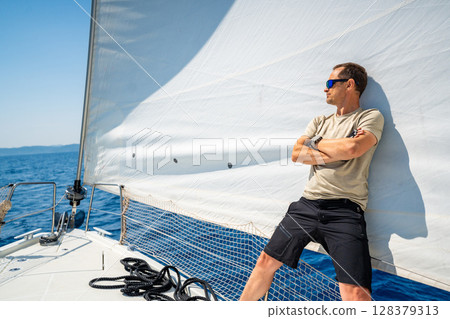 Man leaning on full sails of a sailing yacht in the open sea near Croatia. Masculinity, leadership, yachting and freedom on the water. 128379313