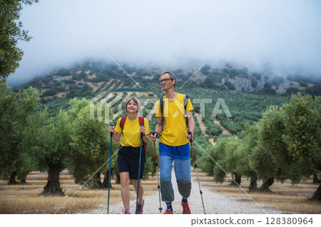 Enthusiastic Couple Hiking Through a Scenic Olive Grove on a Misty Morning, enjoying their outdoor adventure and healthy lifestyle. Enthusiastic Couple Hiking Through a Scenic Olive Grove on a Misty Morning, enjoying their outdoor adventure and healthy lifestyle. 128380964