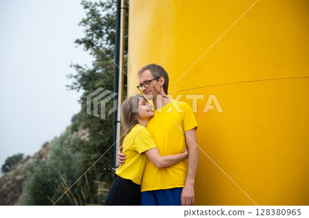 Couple Embracing in Matching Yellow Outfits by a Vibrant Yellow Wall Outdoors 128380965